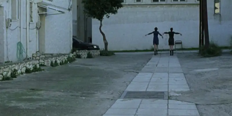 A scene from Attenberg where Marina and Bella are mucking around on a paved footpath