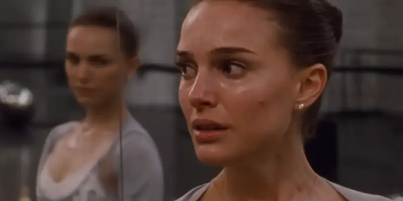 Nina in Black Swan, standing near a mirror looking fearful, her reflection stares back at her with consternation