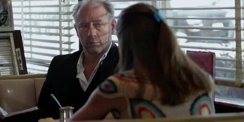 A scene from The Booth at the End where The Man sits in a booth in a cafeteria talking with a woman