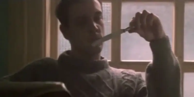 A scene from Wilbur Wants to Kill Himself showing Wilbur sitting at a table holding a table knife