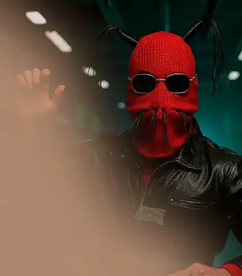 A rendition of Zak Lylak in a strange warehouse. He is wearing red balaclava and leatherette tassels, sunglasses, and a leatherette jacket held together with masking tape.